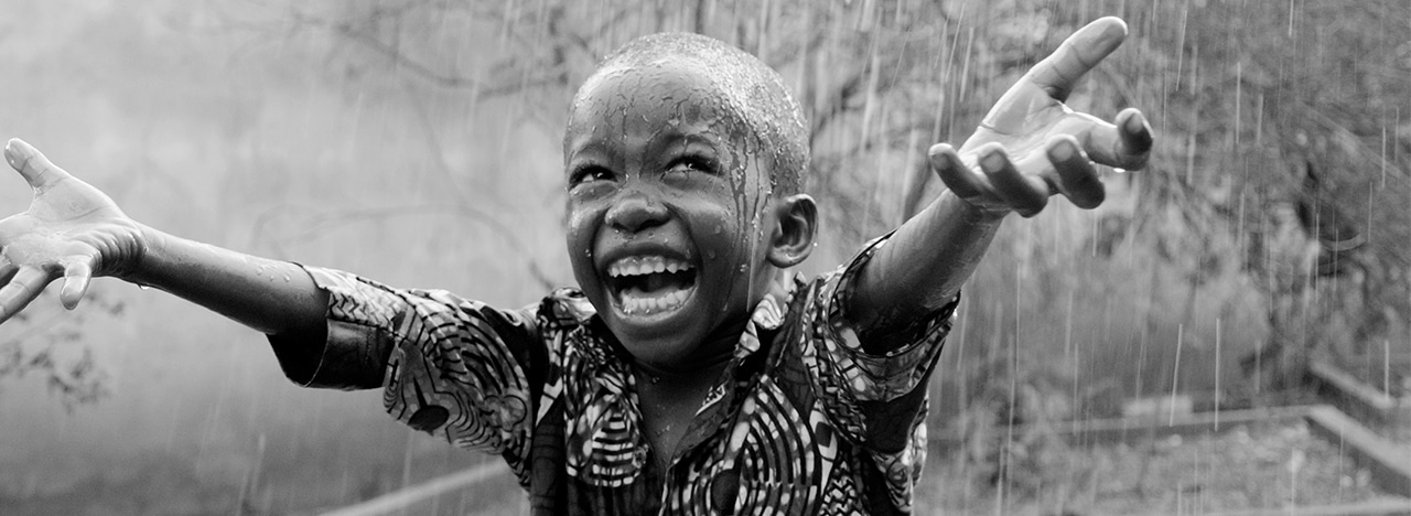 Kid reaching his hands out in pouring rain in Africa, associated to Grieg Foundation.
